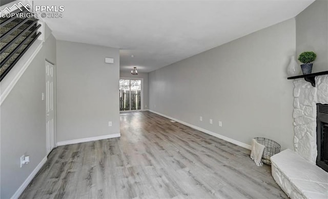 unfurnished living room with wood-type flooring and a stone fireplace