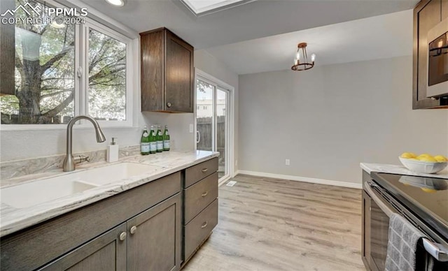 kitchen with light hardwood / wood-style floors, light stone counters, sink, stove, and decorative light fixtures