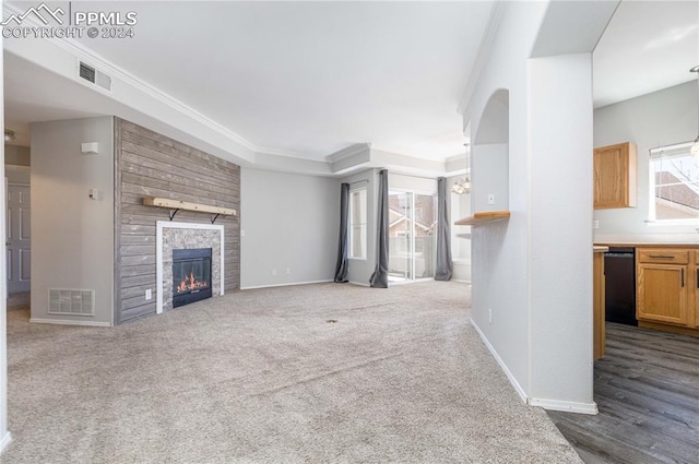 unfurnished living room featuring carpet floors, crown molding, and a stone fireplace