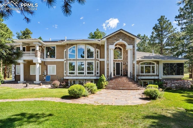 back of property with a yard, stone siding, solar panels, and stucco siding