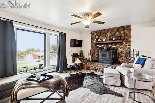 living room featuring light wood-type flooring, ceiling fan, a wood stove, and a fireplace