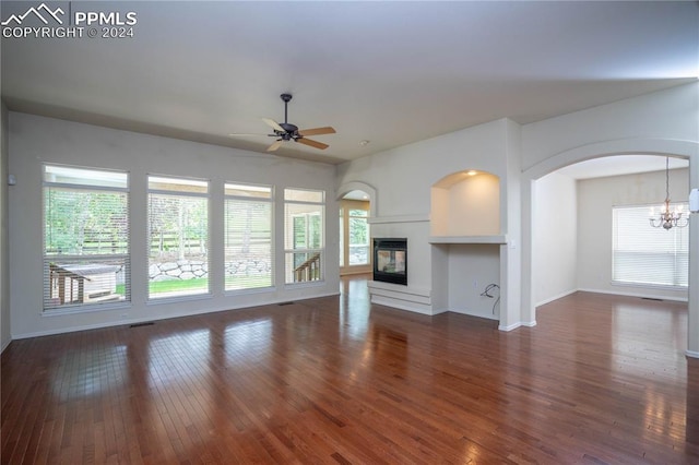 unfurnished living room with dark wood-type flooring, a multi sided fireplace, and ceiling fan with notable chandelier