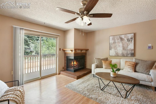 living room featuring ceiling fan, a textured ceiling, a tiled fireplace, and wood-type flooring