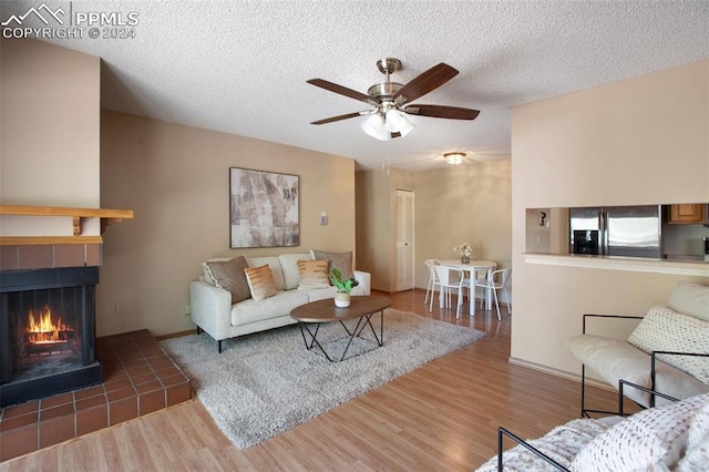 living room featuring ceiling fan, a textured ceiling, a tile fireplace, and wood-type flooring