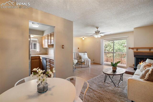 living room with ceiling fan, a fireplace, a textured ceiling, and light hardwood / wood-style floors