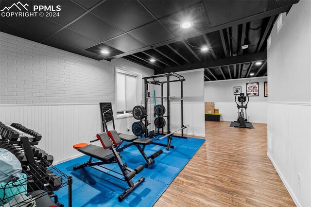 workout area featuring brick wall and wood-type flooring