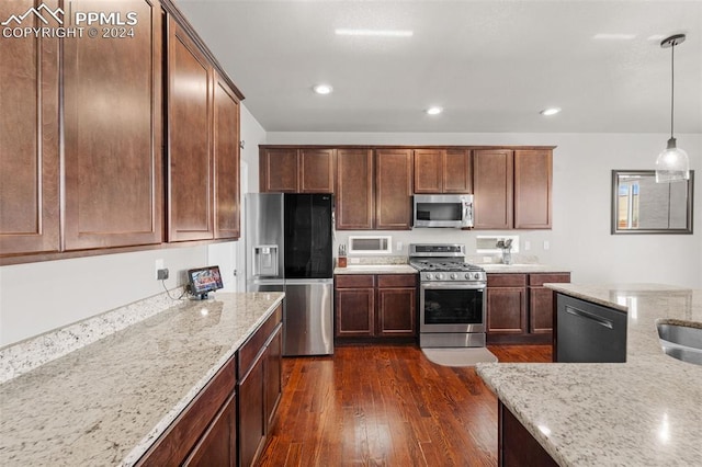 kitchen with appliances with stainless steel finishes, dark wood-type flooring, pendant lighting, and light stone counters