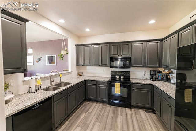 kitchen featuring sink, light stone counters, light hardwood / wood-style floors, and black appliances