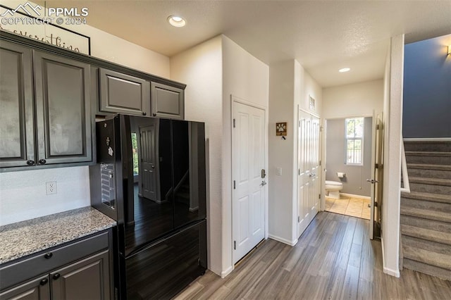 kitchen featuring dark hardwood / wood-style flooring, light stone countertops, and black fridge with ice dispenser