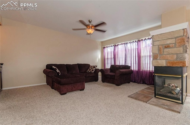 carpeted living room featuring a stone fireplace and ceiling fan