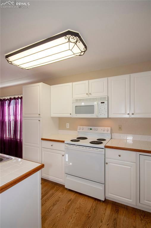 kitchen with white cabinets, light wood-type flooring, tile countertops, and white appliances