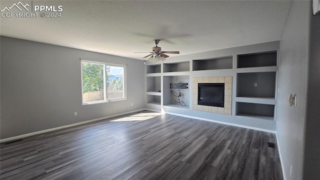 unfurnished living room with a fireplace, built in features, a textured ceiling, ceiling fan, and dark hardwood / wood-style floors