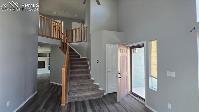 entrance foyer featuring a tiled fireplace, ceiling fan, a high ceiling, and dark hardwood / wood-style flooring