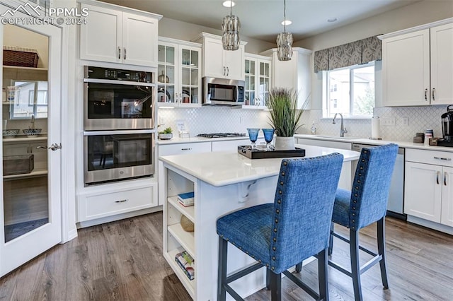 kitchen featuring decorative backsplash, a kitchen island, hanging light fixtures, wood-type flooring, and stainless steel appliances