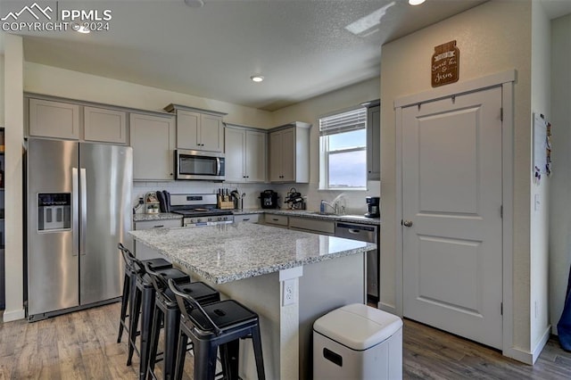 kitchen featuring a kitchen island, stainless steel appliances, hardwood / wood-style flooring, and light stone counters