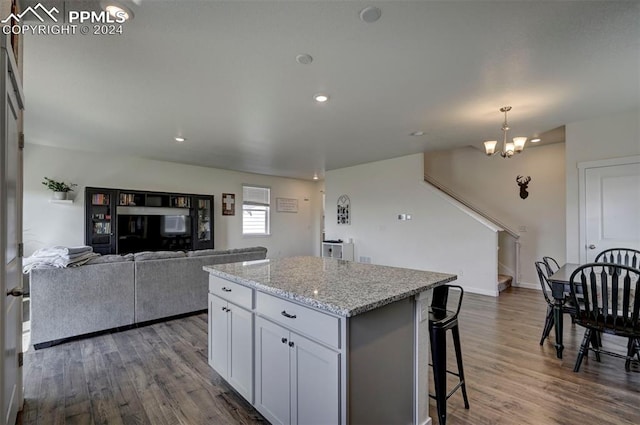 kitchen with a kitchen bar, a center island, a notable chandelier, hardwood / wood-style flooring, and light stone countertops