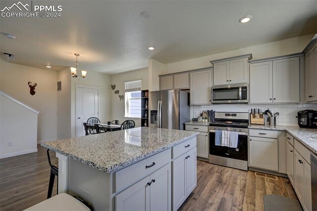 kitchen with stainless steel appliances, hardwood / wood-style floors, tasteful backsplash, light stone countertops, and gray cabinets