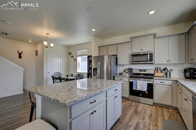 kitchen featuring wood finished floors, appliances with stainless steel finishes, gray cabinets, a center island, and tasteful backsplash