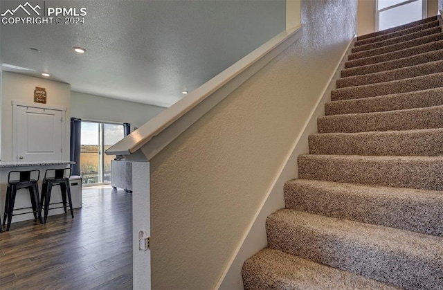 staircase with a textured ceiling, wood finished floors, and a textured wall