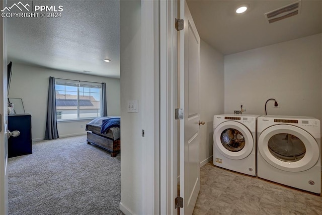 laundry area with light colored carpet, a textured ceiling, and washer and clothes dryer