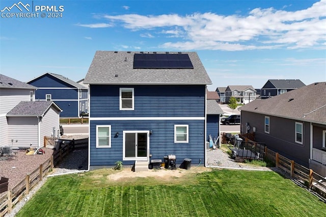 back of house with a fenced backyard, solar panels, a yard, roof with shingles, and a residential view