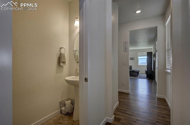 corridor with a textured wall, wood finished floors, and baseboards