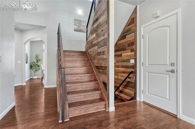 stairway featuring baseboards, arched walkways, and wood finished floors