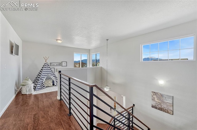 corridor with an upstairs landing, a textured ceiling, baseboards, and wood finished floors