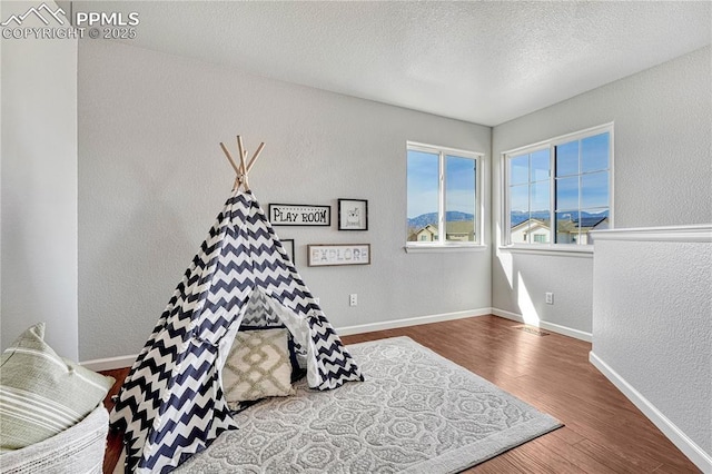 playroom with baseboards, a textured ceiling, wood finished floors, and a textured wall