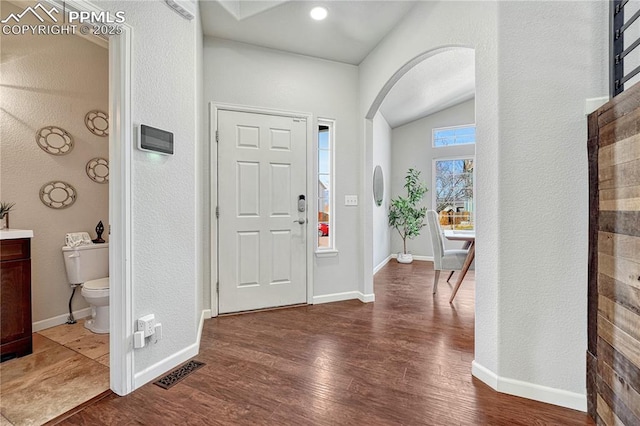 foyer entrance featuring dark wood finished floors, visible vents, arched walkways, and baseboards