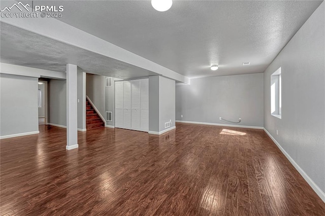 basement featuring visible vents, a textured ceiling, stairway, baseboards, and dark wood-style flooring