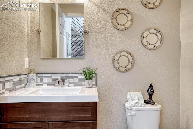 half bathroom featuring toilet, vanity, and a textured wall