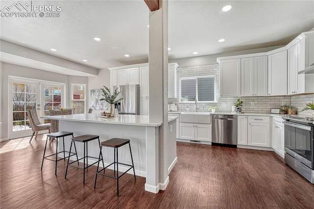 kitchen with a breakfast bar, dark wood finished floors, a sink, decorative backsplash, and stainless steel appliances