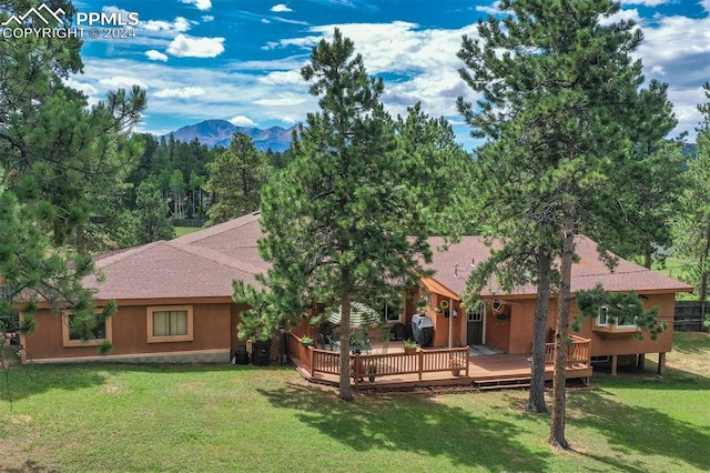 rear view of property with a deck with mountain view and a lawn