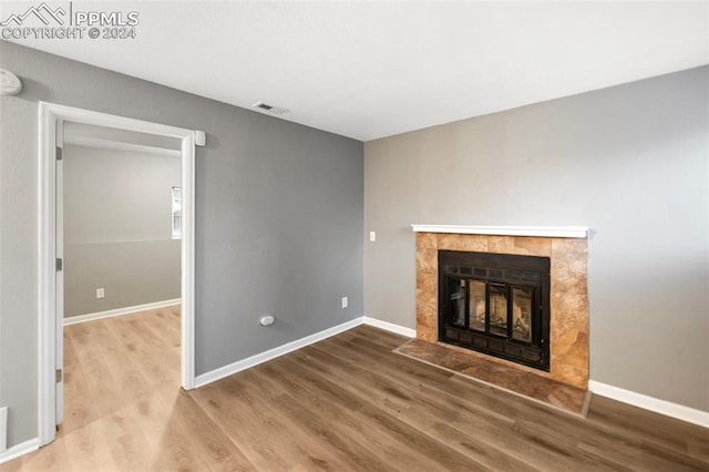 unfurnished living room with hardwood / wood-style floors and a tiled fireplace