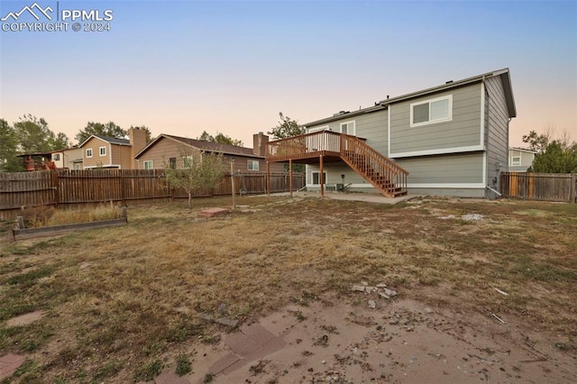 back house at dusk with a wooden deck and a yard