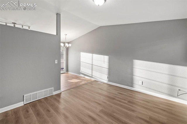 unfurnished living room featuring vaulted ceiling, a notable chandelier, and wood-type flooring