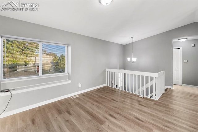 unfurnished room featuring lofted ceiling, a chandelier, and wood-type flooring