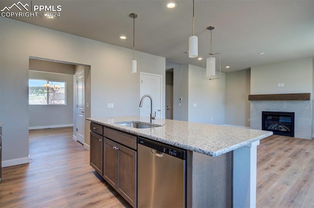 kitchen with light wood-type flooring, stainless steel dishwasher, hanging light fixtures, a tiled fireplace, and sink