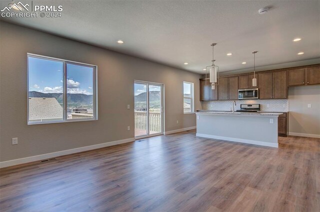 kitchen featuring stove, light hardwood / wood-style flooring, tasteful backsplash, and hanging light fixtures