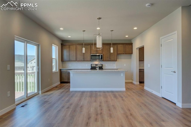 kitchen with decorative backsplash, range, light wood-type flooring, a kitchen island with sink, and hanging light fixtures