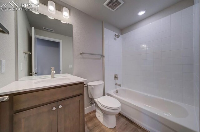 full bathroom with hardwood / wood-style flooring, tiled shower / bath, vanity, and toilet