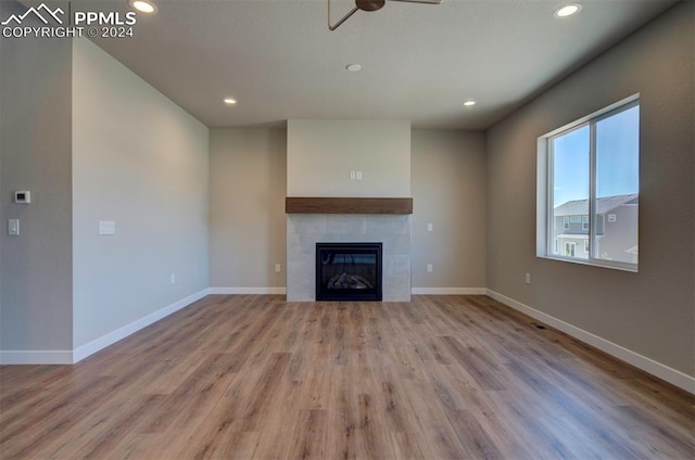 unfurnished living room with ceiling fan, a tiled fireplace, and hardwood / wood-style flooring