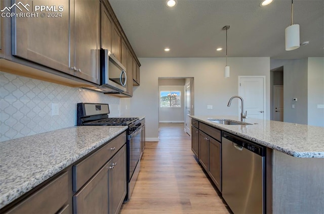 kitchen with light wood-type flooring, backsplash, appliances with stainless steel finishes, sink, and a center island with sink