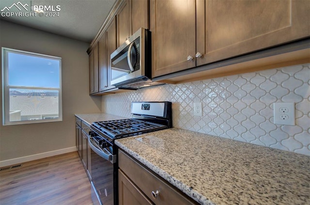 kitchen with light hardwood / wood-style flooring, backsplash, light stone countertops, and gas stove