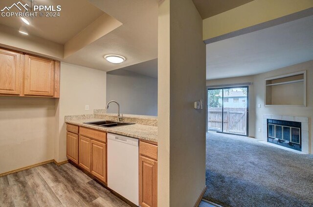 kitchen featuring dishwasher, sink, light stone counters, a fireplace, and light carpet