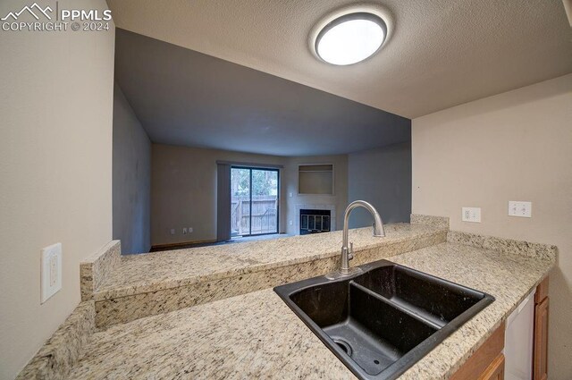 kitchen with sink, a textured ceiling, light stone counters, and white dishwasher