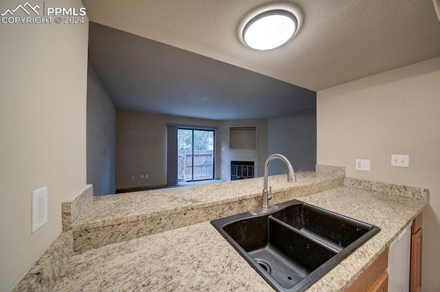 kitchen with a textured ceiling, a fireplace, a sink, open floor plan, and stainless steel dishwasher