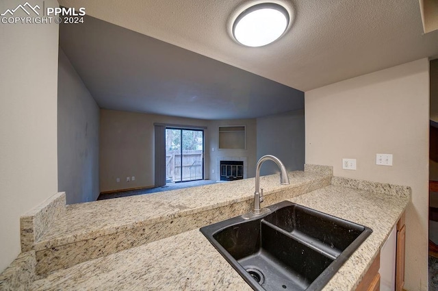 kitchen with sink, light stone counters, and a textured ceiling