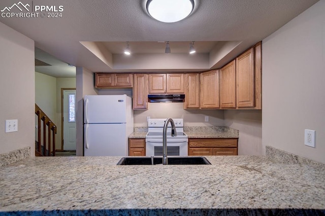 kitchen with a raised ceiling, range, light stone countertops, extractor fan, and white refrigerator